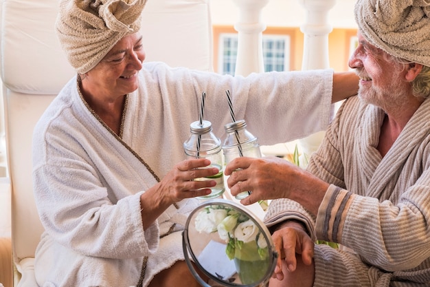 Paar senioren in een schoonheidssalon die samen een cocktail nemen met room op het gezicht van de volwassen man - twee gepensioneerden in een schoonheidssalon