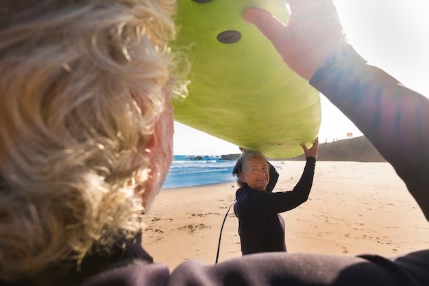 Paar senioren klaar om te gaan surfen op het strand met een grote groene surftafel bij elkaar - proberen hun eerste keer in een surfles in hun vakantie