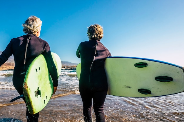 Paar senioren op het strand met zwarte wetsuits met een surftafel klaar om te gaan surfen op het strand - actieve volwassen en gepensioneerde mensen die samen gelukkige activiteiten doen in hun vakantie of vrije tijd