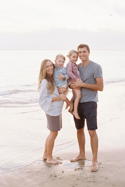 Paar staan met hun zoon en dochter op een zandstrand aan de oceaan en kijken naar de camera glimlachend