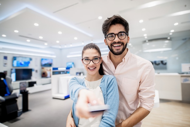 Paar staande in tech winkel. In meisjeshand afstandsbediening voor plasma tv. Nieuwe technologieënconcept.