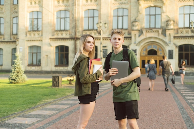 paar studenten met boeken en een laptop in hun handen staan op de achtergrond van het hoofdgebouw