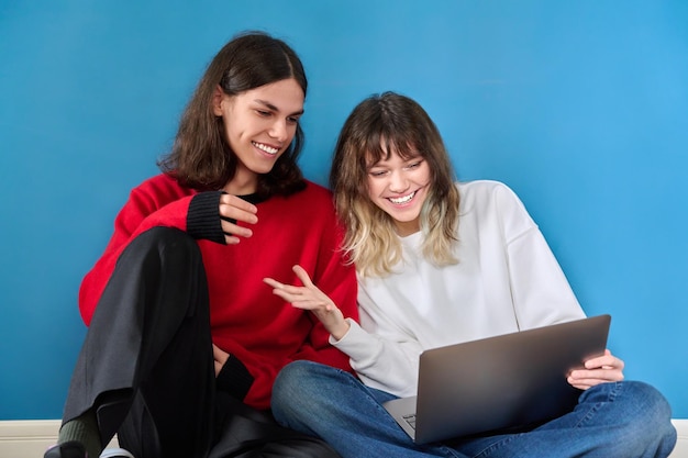 Paar tiener studenten met behulp van laptop zittend op de vloer op blauwe achtergrond