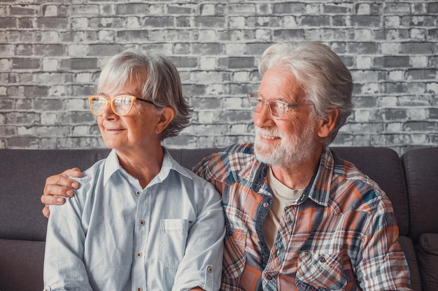 Foto paar twee mooie en schattige senioren thuis zittend op de bank kijkend naar het raam met een bril samenxa