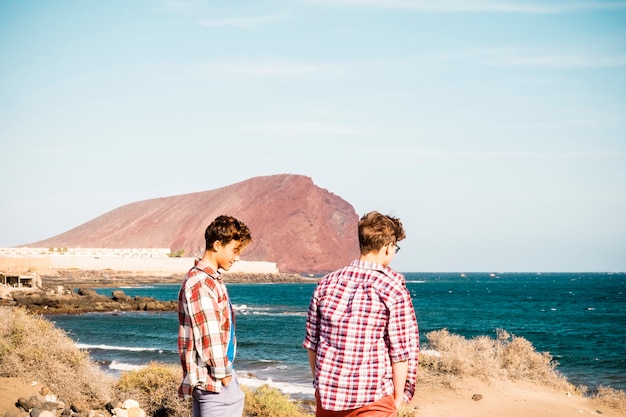 Paar twee tieners met een vriendschap op het strand die naar de zee kijken en samen praten - zee of oceaan op de achtergrond