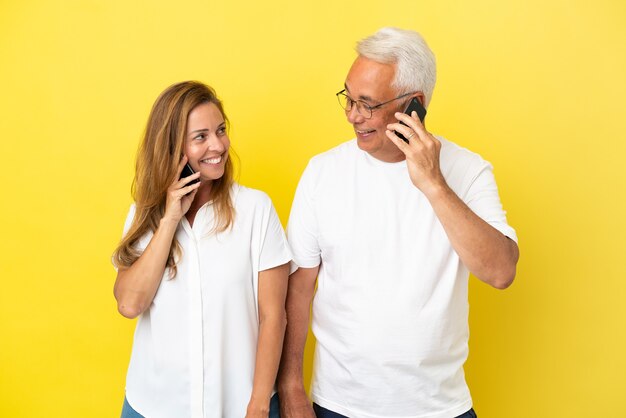 Paar van middelbare leeftijd geïsoleerd op gele achtergrond praten met mobiel