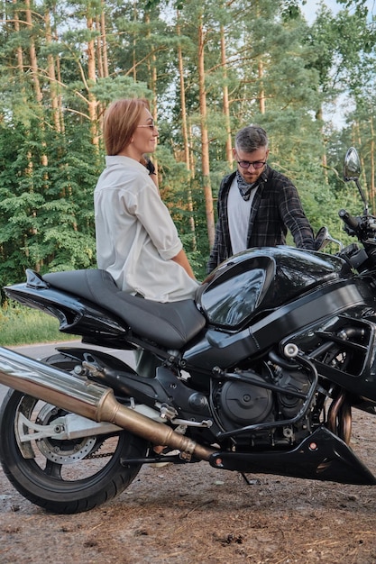 Paar van middelbare leeftijd praten en plezier hebben zittend op een motorfiets die samen op een bosweg reist