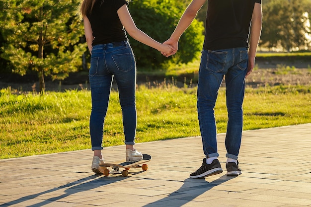 Paar verliefd in een zomerpark. benen (voeten) van een man en een vrouw in modieuze jeans en stijlvolle sneakers op een skateboard (longboard) voetpad asfalt. jeugdactiviteit en het eerste liefdesconcept