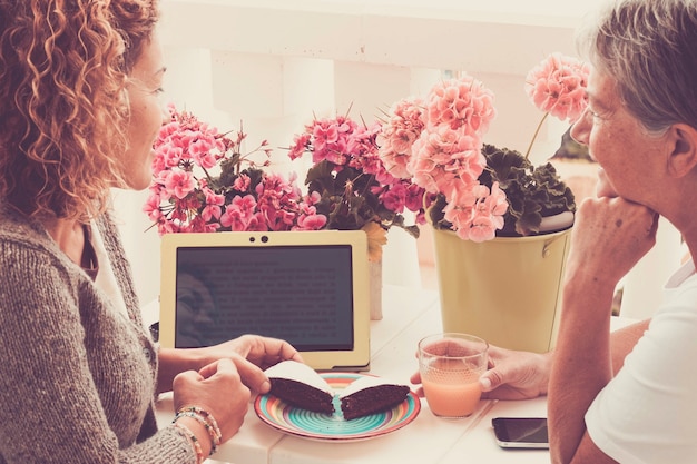 Paar vrienden vrouwen midden en derde leeftijd 40 en 70 jaar oud blijven samen in gelukkige vrijetijdsbesteding middag eten wat cake en drinken fruit iets lezen op laptop en een mobiele telefoon op tafel