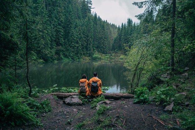 Paar wandelaars in gele regenjas kijken naar bergmeer backpackers