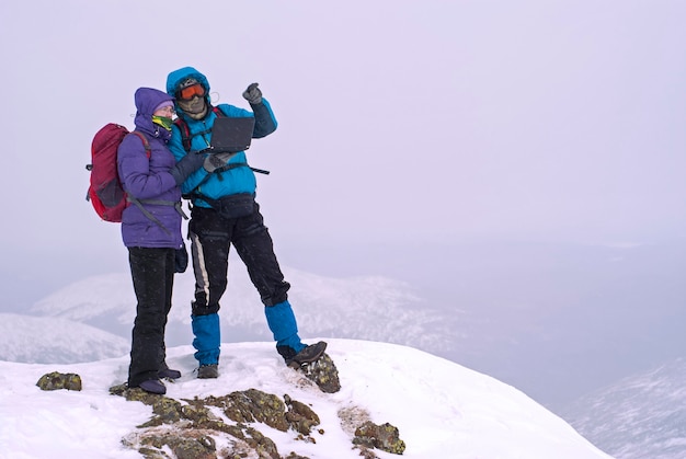 Paar wandelaars op een winterbergtop met een laptop