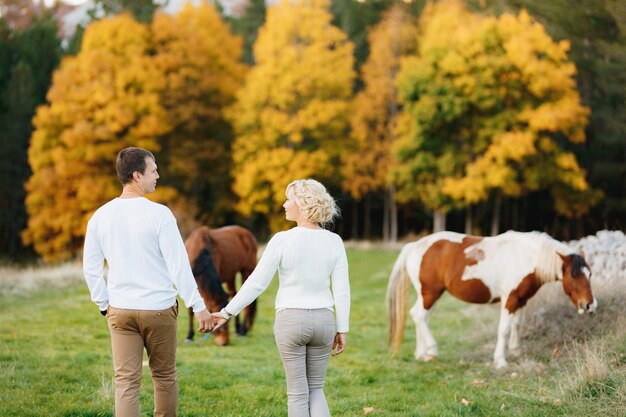 Paar wandelingen op het gazon in de herfst bos hand in hand paarden grazen op het gazon achteraanzicht