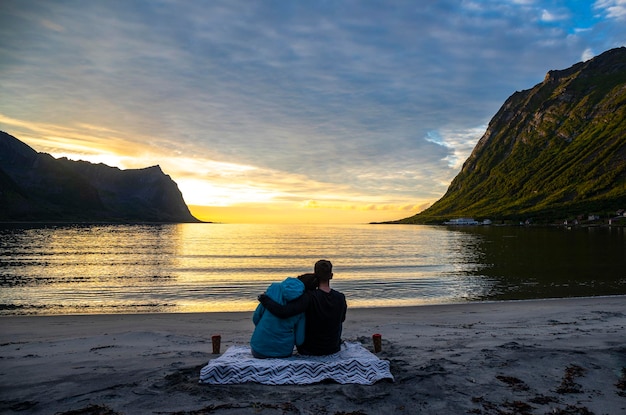 paar zittend op een deken op het strand genietend van een romantische zonsondergang in de Noorse fjord, senja