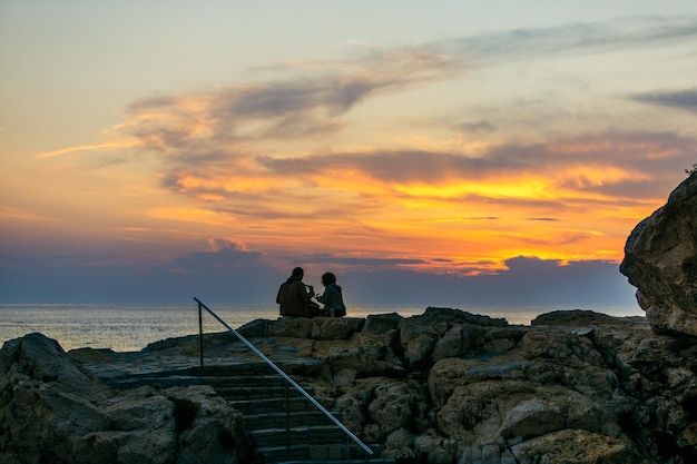 Paar zittend op een rotsachtige klif op zoek op zonsondergang romantische datum zomervakantie