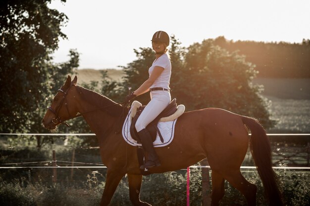 Paardrijden opleiding in de frisse lucht op zomeravond. mooie jonge vrouw in witte sport uniform.