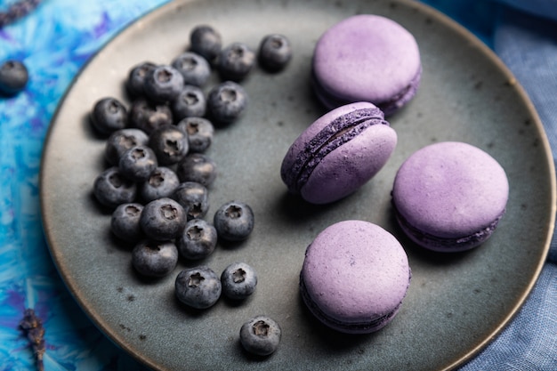 Paarse macarons of bitterkoekjes taarten met bosbessen op keramische plaat op een blauwe betonnen achtergrond.