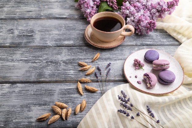 Paarse macarons of bitterkoekjes taarten met kopje koffie op een grijze houten achtergrond en wit linnen textiel. Zijaanzicht,