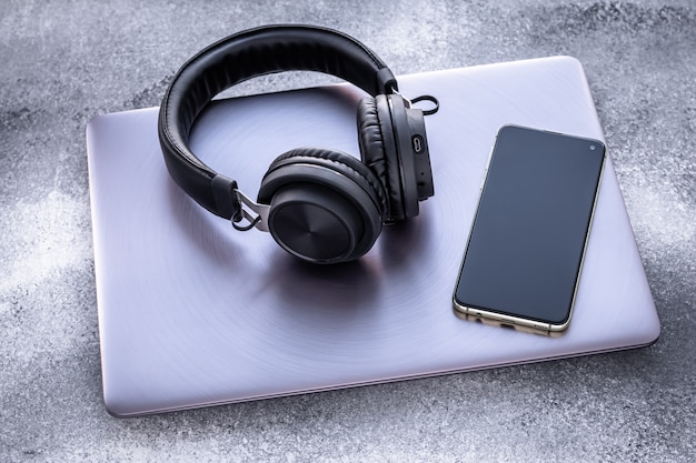Paarse metalen laptop, zwarte draagbare hoofdtelefoon en mobiele telefoon op grunge grijze achtergrond. Sociaal isolement, levensstijl.