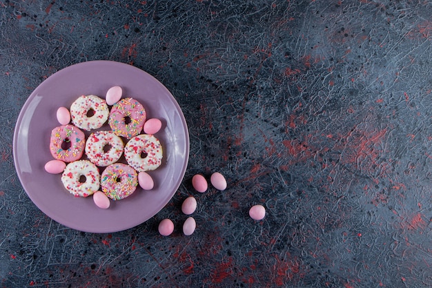 Paarse plaat van kleurrijke heerlijke donuts op donkere ondergrond.