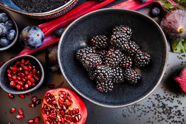 Paarse rauwe groenten en fruit op zwarte achtergrond en bramen op een kom