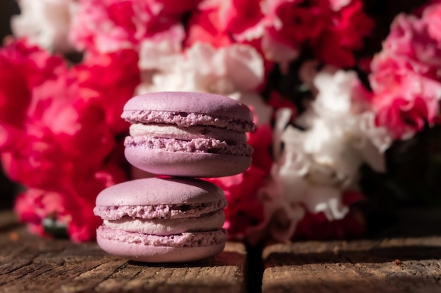 Paarse romige bitterkoekjes op het houten bord roze boeket bloemen op de achtergrond