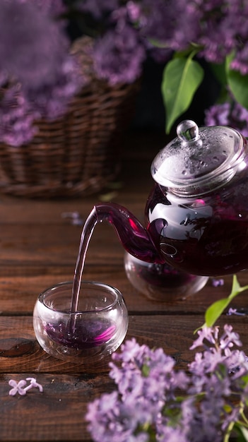 Paarse thee wordt uit een glazen theepot in kopjes gegoten lila bloemen zijn overal aanwezig