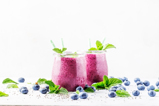 Paarse zelfgemaakte yoghurt of smoothie met bosbessen chia zaden en muntblaadjes in glazen potten op grijze achtergrond selectieve focus