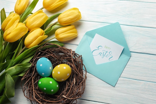 Paasachtergrond met felgekleurde eieren in nest en gele tulpen Bovenaanzicht met kopieerruimte