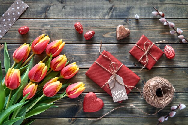 Paasarrangement: rode tulpen, ingepakte cadeautjes, koord en decoratieve hartjes op houten tabke, plat gelegd