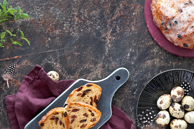 Paasbrood (osterbrot in het duits). bovenaanzicht van traditionele fruitige brood op donkere tafel met verse bladeren en kwarteleitjes. kopie-ruimte.