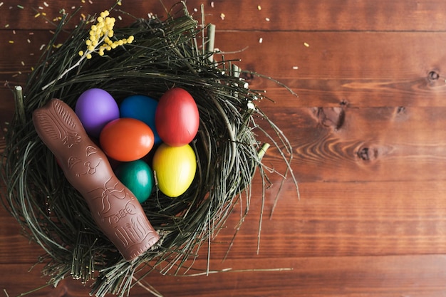 Paaseieren en chocoladekonijntje in een nest van takken op donkere houten achtergrond Kopieer ruimte Bovenaanzicht