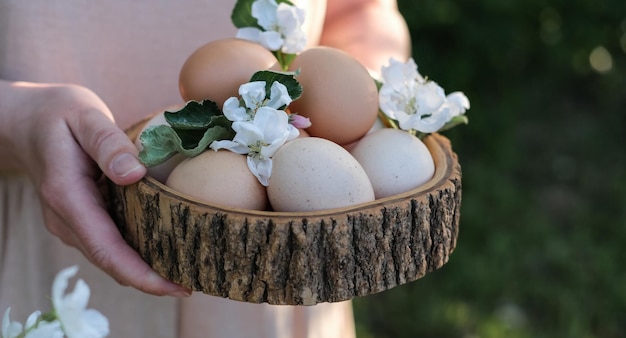 Paaseieren en lentebloemen in houten kom in vrouwelijke handen Pasen in rustieke stijl