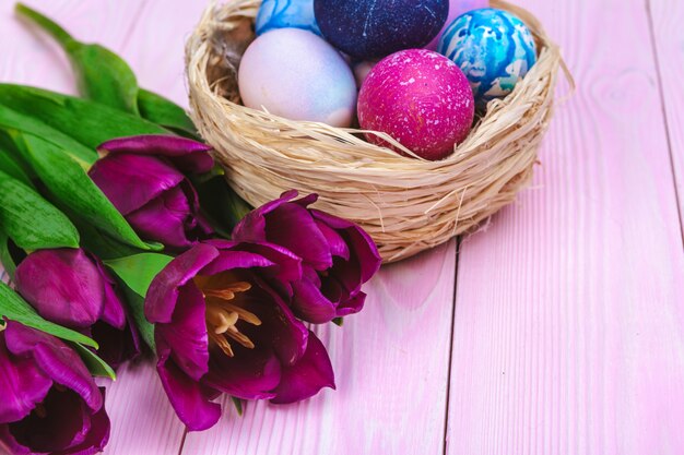 Paaseieren in een nest en tulpen op houten planken