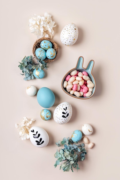 Paaseieren met snoep en bloemen op beige Happy Easter-concept Witte en blauwe eieren met schattig bord in de vorm van een konijntje