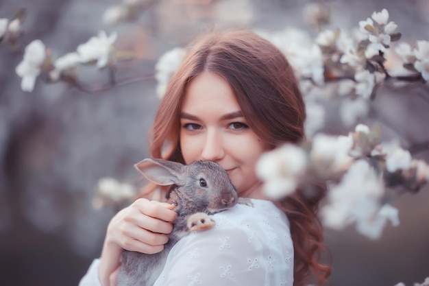 paashaas in de handen van een mooi meisje, lente, april in een bloeiende tuin, portret van een vrouw