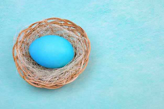 Paaskaart met een blauwgroen paasei in een rieten mand op blauw