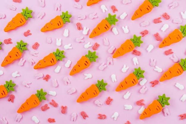 Paaspatroon gemaakt van decoratie met konijnenoren, suiker en oranje wortel op roze achtergrond