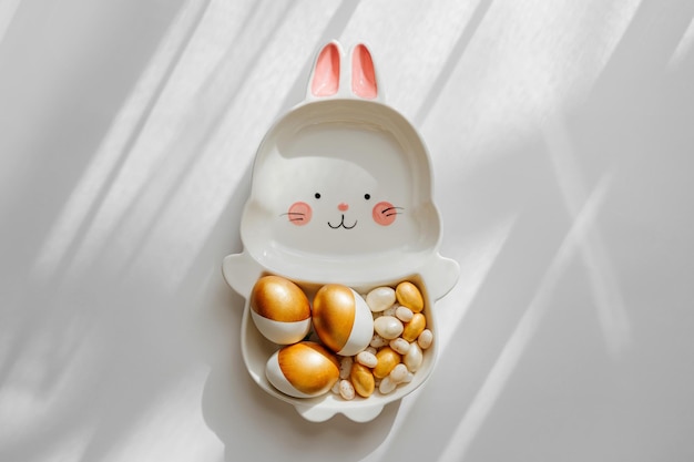 Paastafeldecoratie met schattig bord in de vorm van een konijntje met gouden paaseieren en snoep Gelukkig paasconcept Idee voor het paasdiner