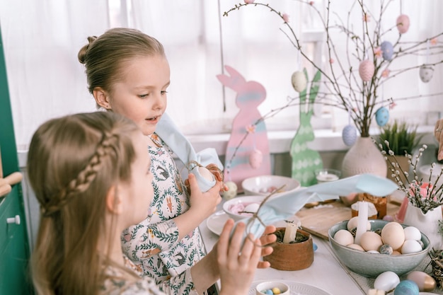 Foto paasvakantie in het lenteseizoen gelukkige familie openhartige kleine kinderen zusters meisjes hebben plezier thuis tafel versieren met eieren in servet zoals oren konijn traditioneel eten feestelijk huisdecor