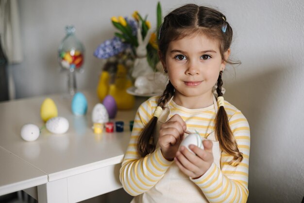 Paasvakantie thuis Portret van een schattig klein meisje dat eieren in de keuken schildert