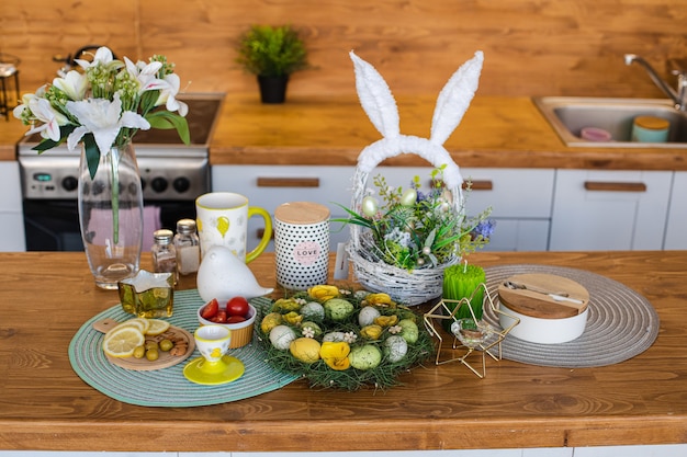 Paasviering op houten aanrecht. Geverfde eieren met snacks en mand met konijnenoren op houten aanrecht.