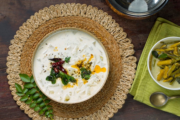 Pachadi or Raitha and olanKerala feast side dishes vegeterian food  items arranged in a brass vessel  and white bowl which is placed on wooden background