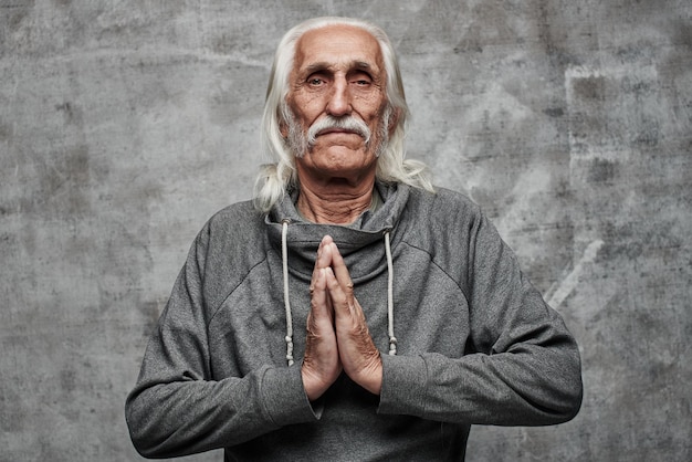 The pacified gray-haired grandfather folded his palms in prayer position, meditation, relaxation, forgiveness, keep calm. Gray studio background