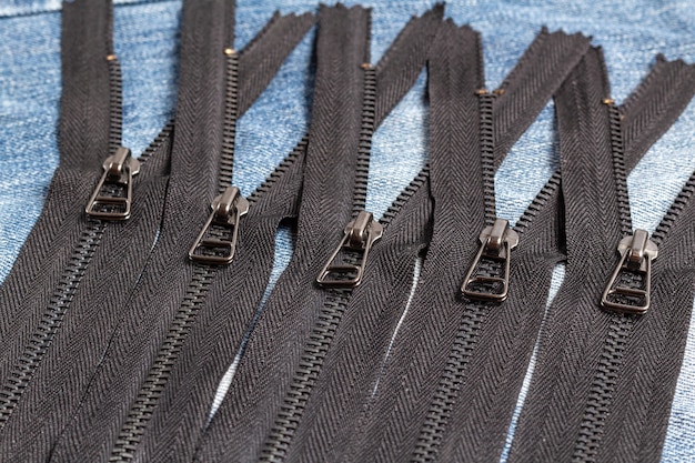 Pack a lot of black metal brass zippers stripes with sliders pattern for handmade sewing tailoring leatherwork leathercraft on the blue wooden background