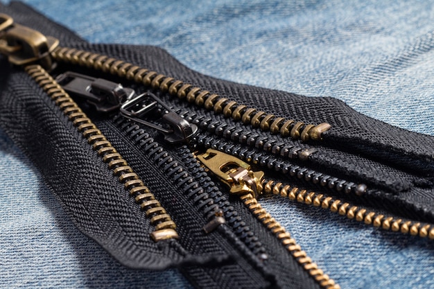 Pack a lot of black metal brass zippers stripes with sliders pattern for handmade sewing tailoring leatherwork leathercraft on the blue wooden background