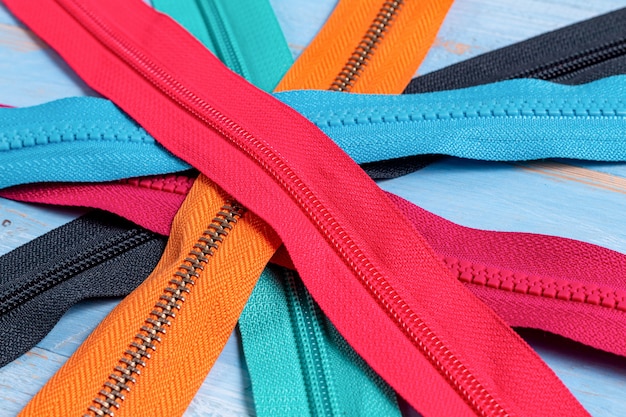 Pack lot of colorful plastic and metal zippers stripes with sliders pattern for handmade sewing tailoring on the blue painted wooden background close up selective focus