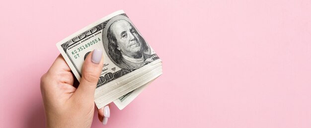 A pack of one hundred dollar bills in female hand on colorful surface. copy space.