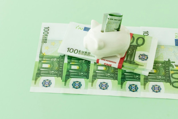 A pack of one hundred euros banknotes in a bank package with a\
piggy bank and a folded banknote in it. the concept of saving