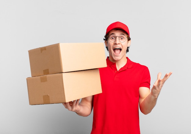 Package deliver boy feeling happy, excited, surprised or shocked, smiling and astonished at something unbelievable