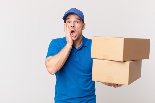 Package deliver man feeling shocked and scared, looking terrified with open mouth and hands on cheeks